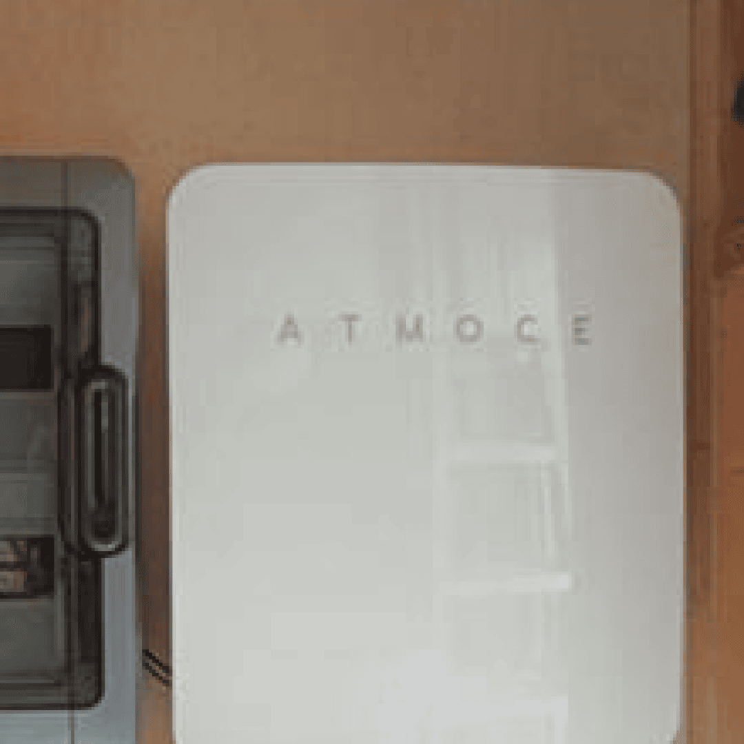 Ein weißes Gerät mit der Aufschrift ATMOCE ist neben einem grauen rechteckigen Gerät an der Wand angebracht. Beide Geräte haben ein schlankes, modernes Design.