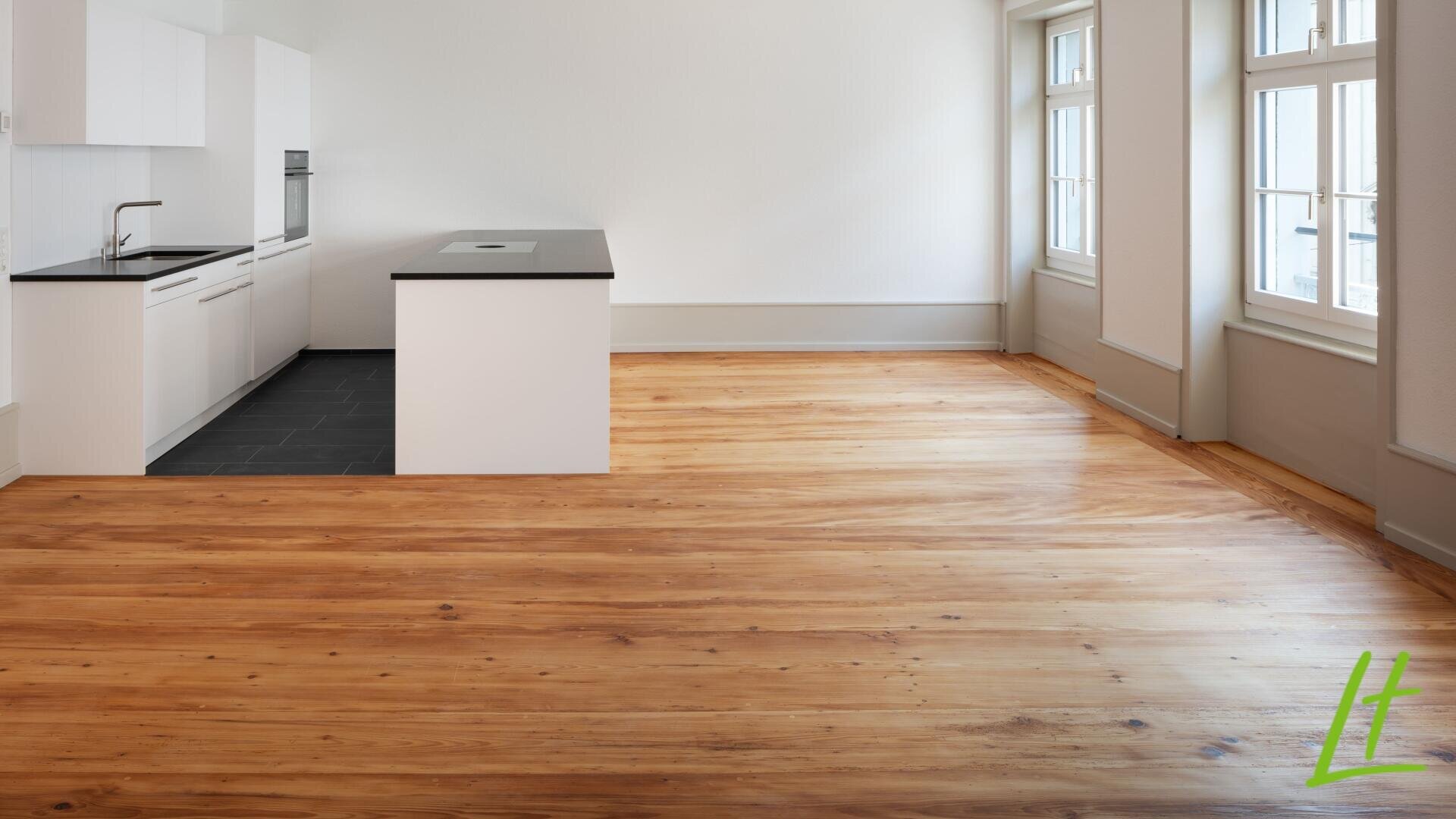 Modernes, unmöbliertes Apartment mit einer Küche mit weißen Schränken, schwarzen Arbeitsflächen, einer zentralen Insel und einem offenen Wohnbereich mit polierten Holzböden und großen Fenstern, die viel Tageslicht hereinlassen.