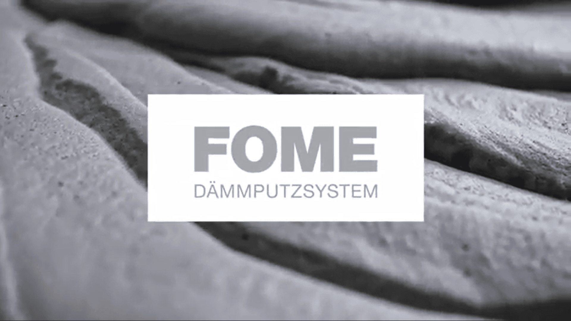 Gros plan sur un matériau gris texturé avec l'inscription FOME SYSTEME D'ENDUCTION en caractères gras, centré sur une superposition rectangulaire blanche.