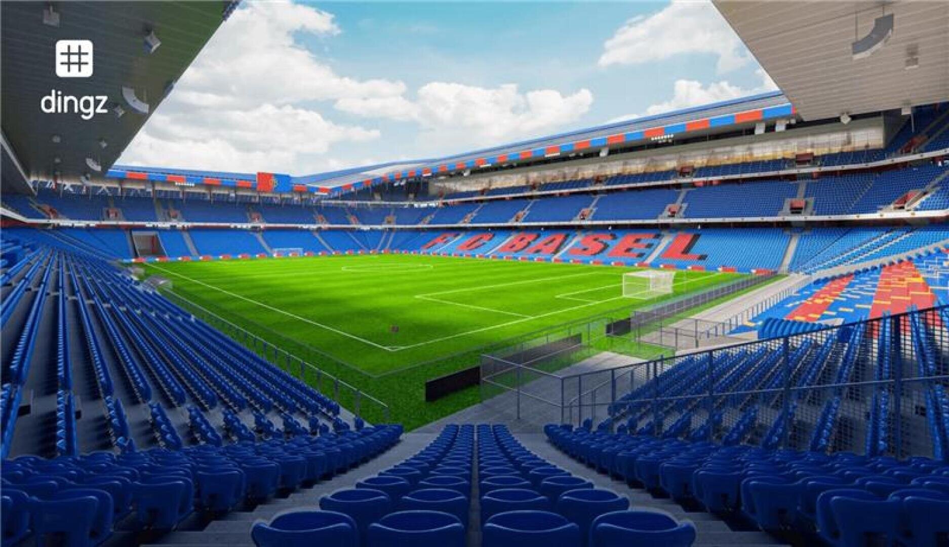 Weitwinkelansicht eines leeren Fussballstadions mit blauen und roten Sitzen, grünem Spielfeld und dem Schriftzug FC BASEL in großen Buchstaben auf der Tribüne. Das Stadion liegt unter einem teilweise bewölkten Himmel.