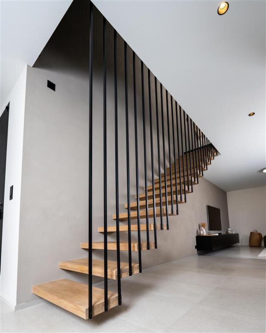 Escalier moderne minimaliste avec des marches en bois flottantes et de fines rampes verticales noires devant un mur gris clair dans un espace de vie contemporain clair et ouvert.