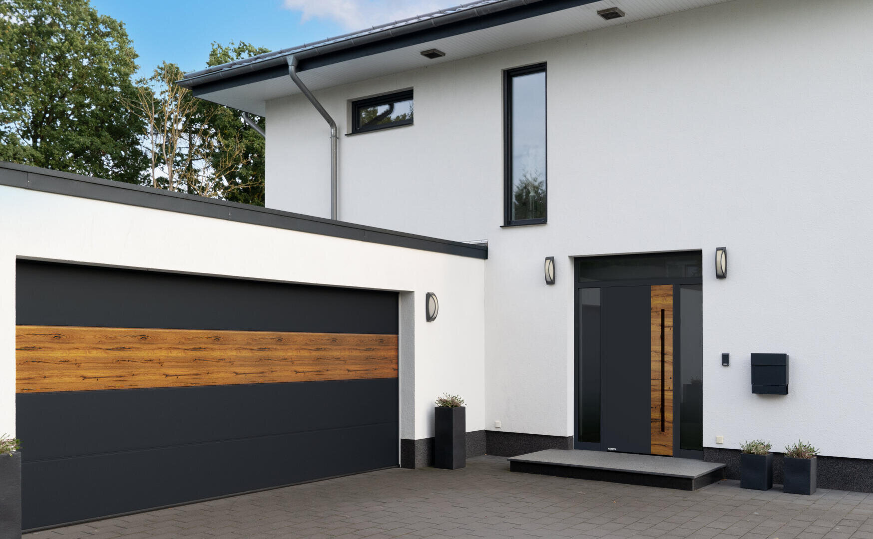 Moderne Hausfassade mit weißen Wänden, einem großen Fenster über der Tür und einem schlichten Garagentor mit einem horizontalen Holzakzent. Der Eingang ist mit minimalistischen Außenleuchten und Topfpflanzen dekoriert.