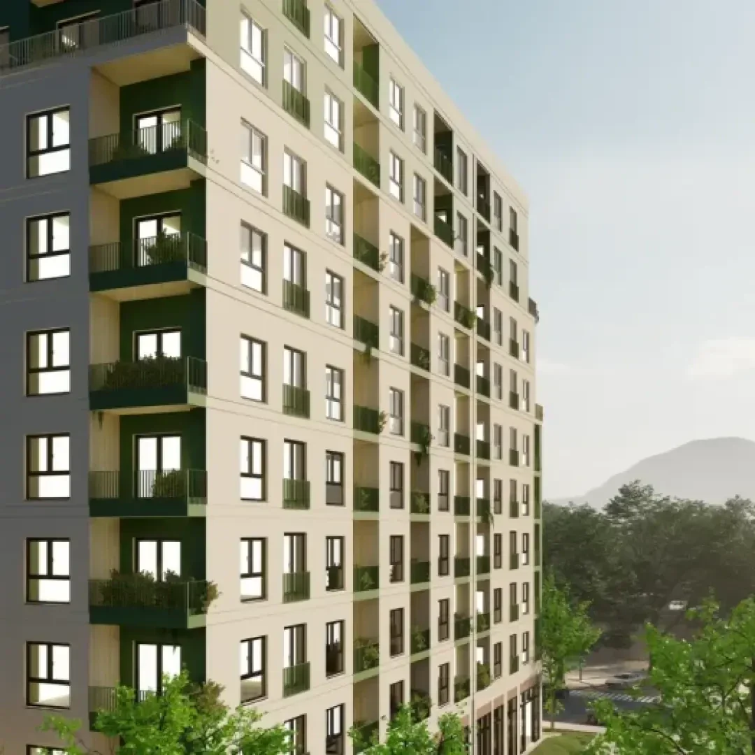 Un immeuble d'habitation moderne à plusieurs étages avec des balcons et de grandes fenêtres, entouré d'arbres verts. Le ciel est dégagé et on aperçoit une colline lointaine en arrière-plan.