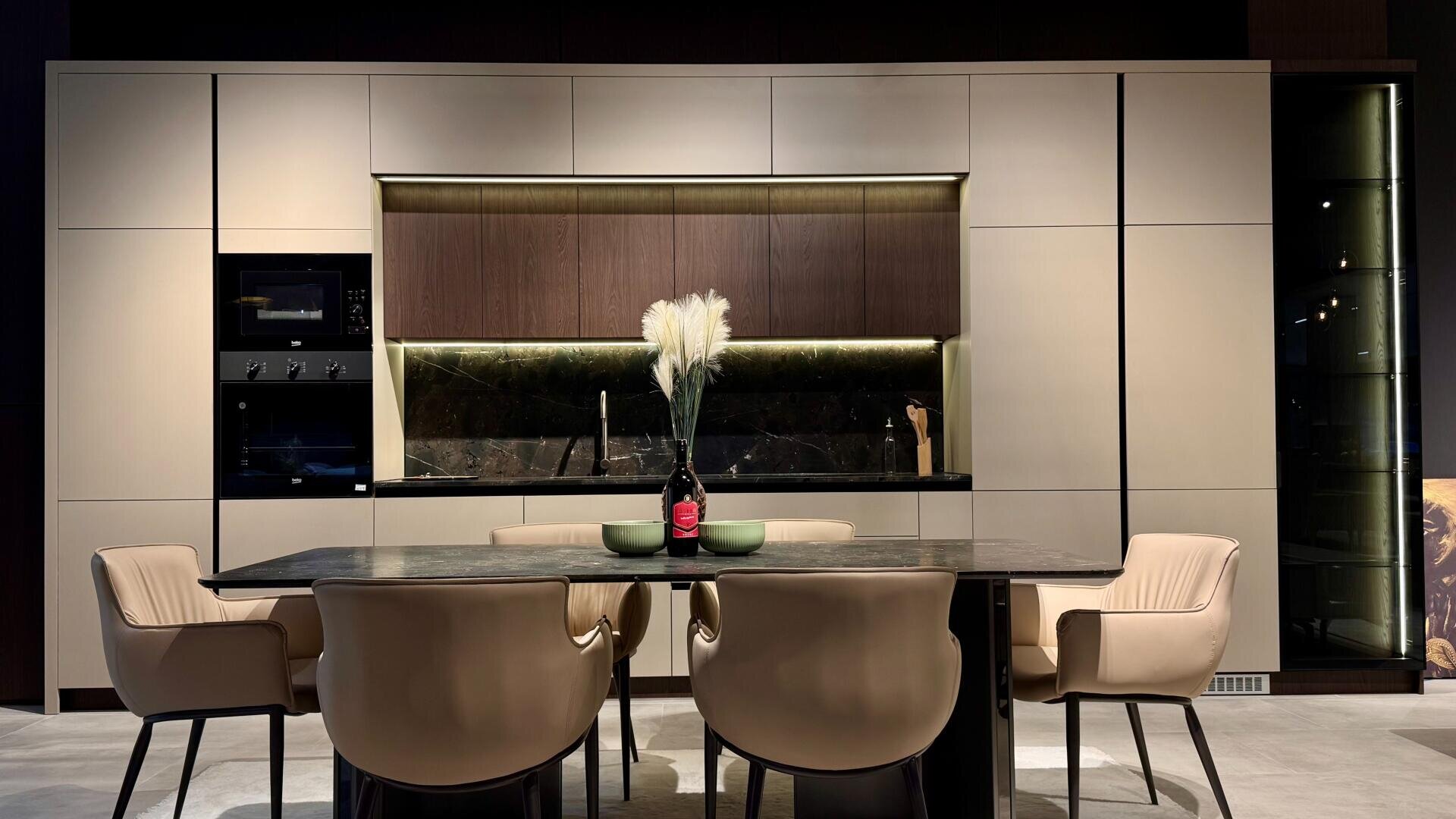 Moderne Küche und Essbereich mit beigen Schränken, schwarzem Marmorsockel, einem Esstisch mit Marmorplatte, fünf beigen Stühlen und einer dekorativen Vase mit weißem Pampasgras als Mittelpunkt.