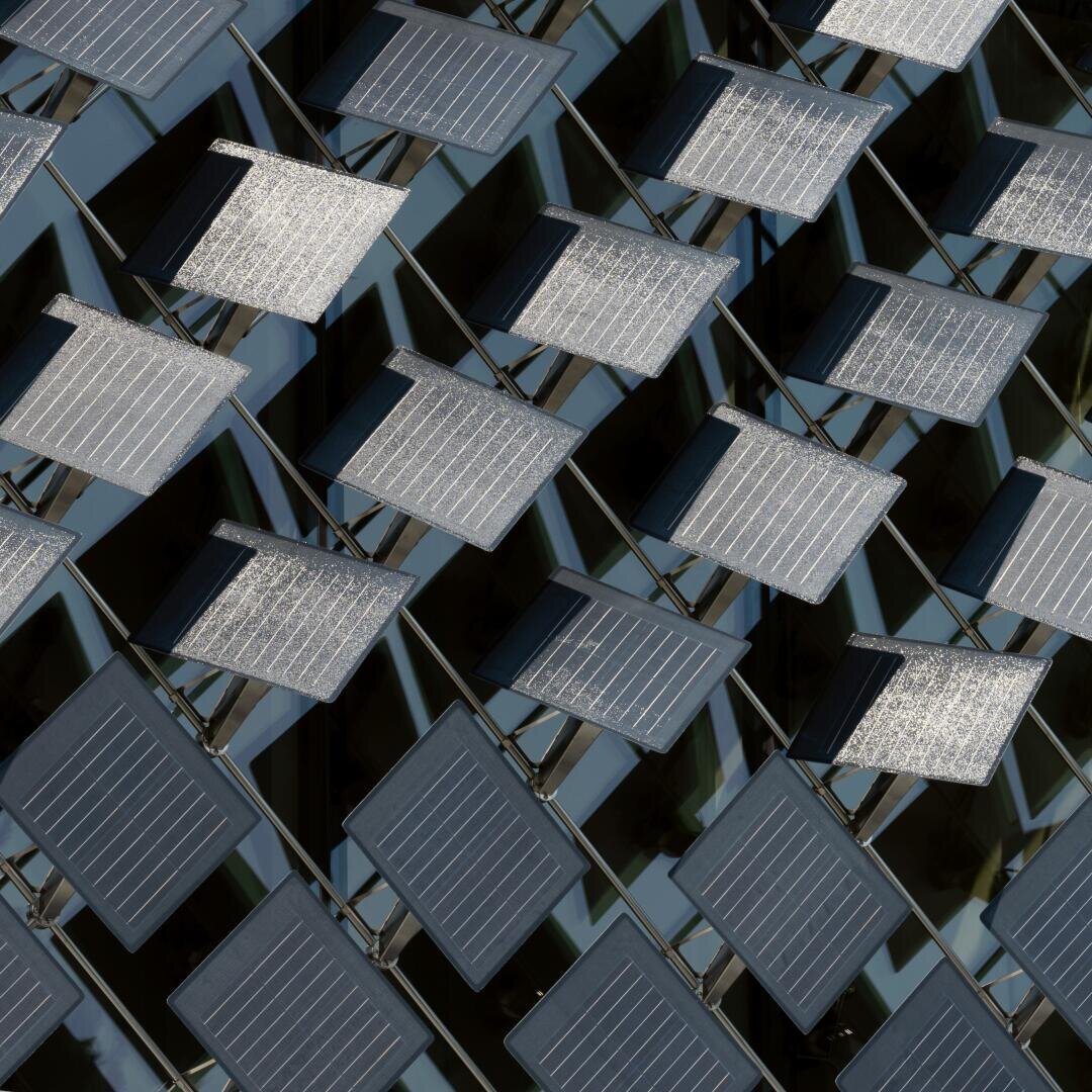 Nahaufnahme mehrerer quadratischer Solarmodule, die in einem diagonalen, gitterartigen Muster an einer Gebäudefassade angeordnet sind, wobei das Sonnenlicht von einigen der Module reflektiert wird.