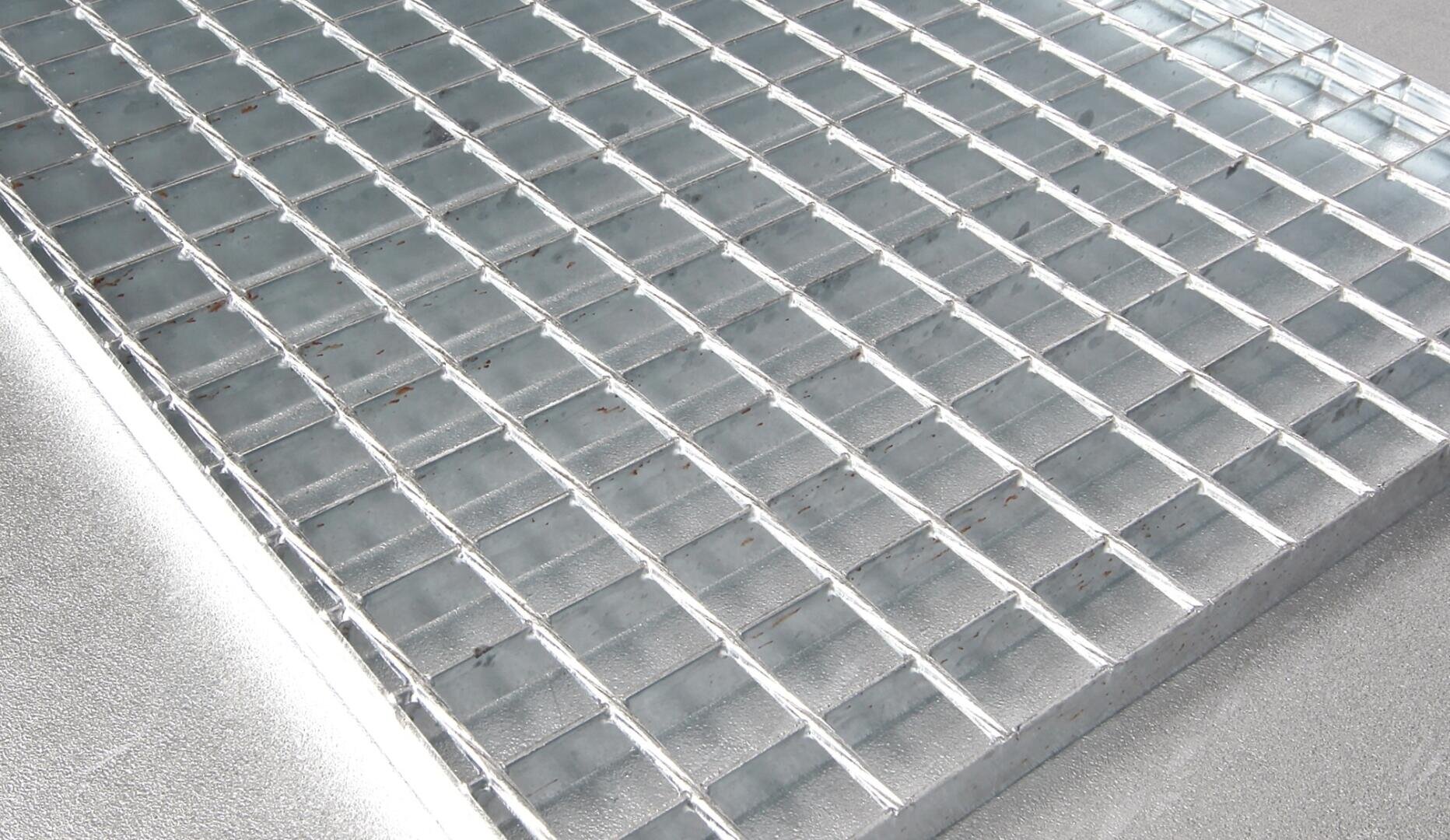 Gros plan d'une grille métallique à motif rectangulaire, vue de biais. La surface apparaît propre et brillante, reflétant la lumière.