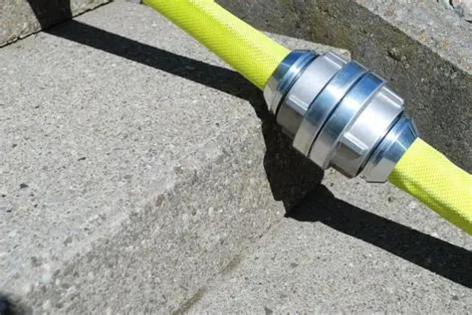 Un tuyau d'incendie jaune vif avec un raccord métallique argenté est posé sur les marches en béton dans la lumière du soleil et projette une ombre.