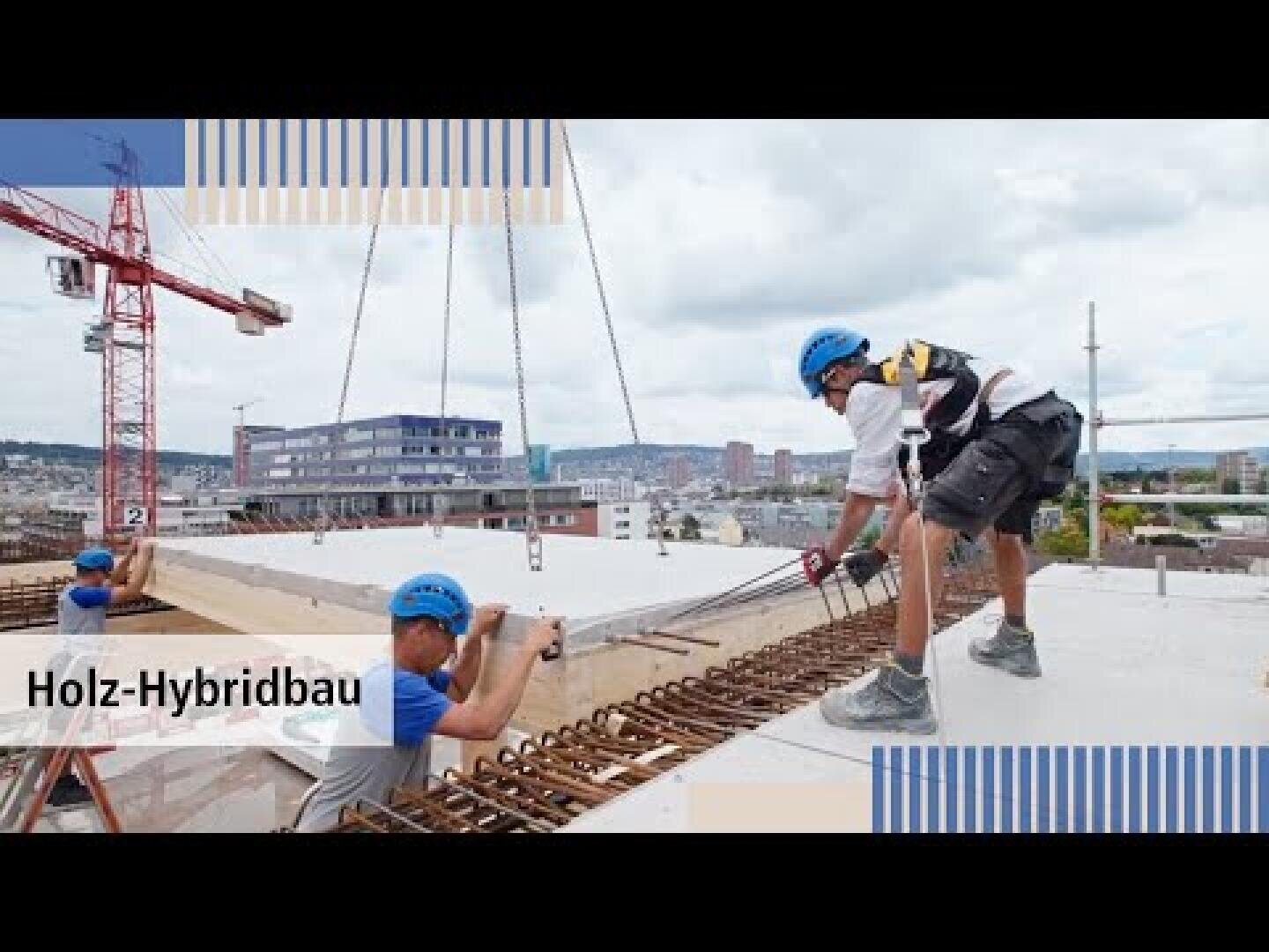 Bauarbeiter mit blauen Helmen führen eine große Holzplatte, die von einem Kran auf einer Baustelle angehoben wird. Im Hintergrund sind städtische Gebäude und ein bewölkter Himmel zu sehen. Der Text auf dem Bild lautet Holz-Hybridbau.