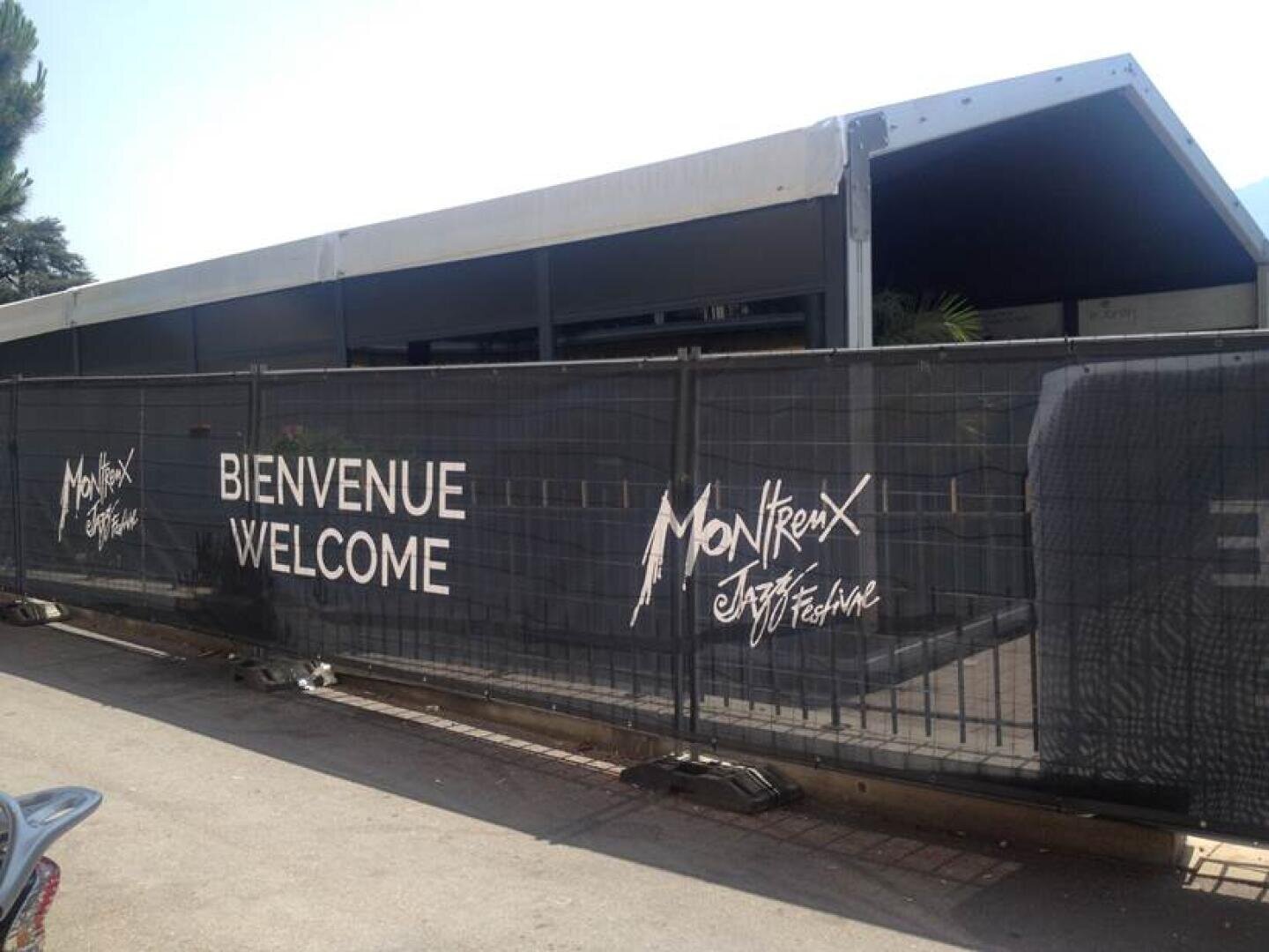 Ein grosses Zelt hinter einem Zaun mit der Aufschrift Bienvenue Welcome und Montreux Jazz Festival in weissen Buchstaben auf schwarzen Bannern.