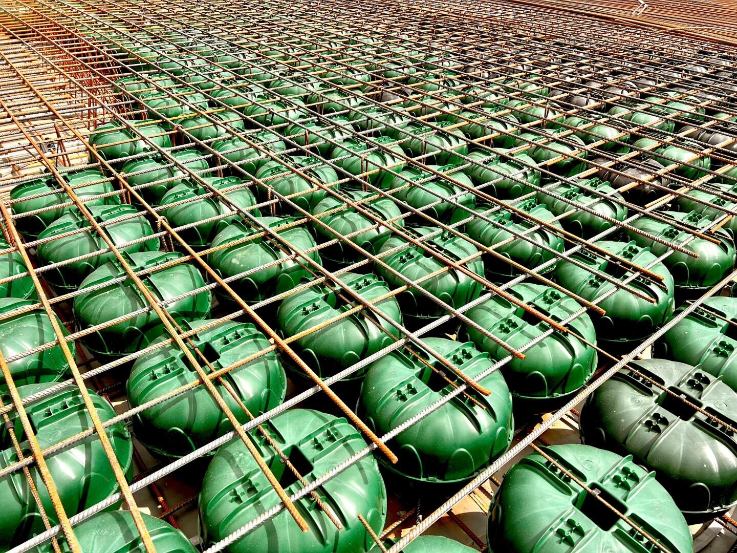 Reihen von grünen Kunststoffkugeln sind in einem Raster unter einem Netz von Stahlstäben angeordnet und bilden einen Teil der Stahlbetonplattenkonstruktion und sparen somit Beton.