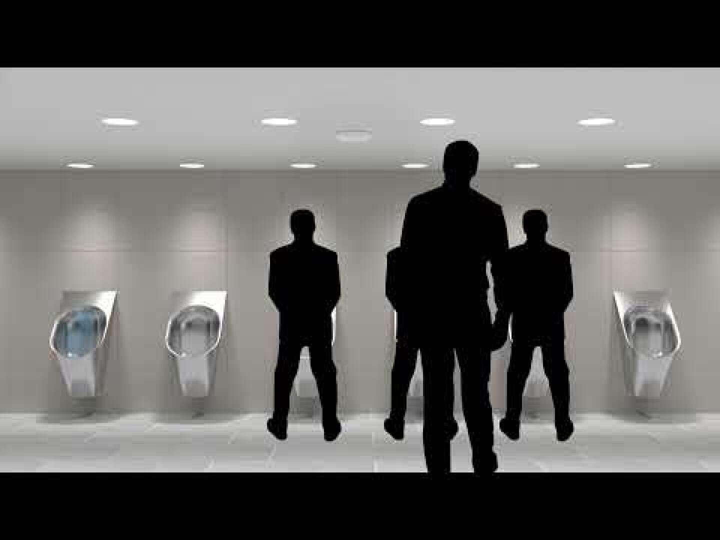 Silhouetten von vier Männern stehen an getrennten Pissoirs in einer modernen, gut beleuchteten öffentlichen Toilette mit gefliestem Boden und schlichten Wänden.