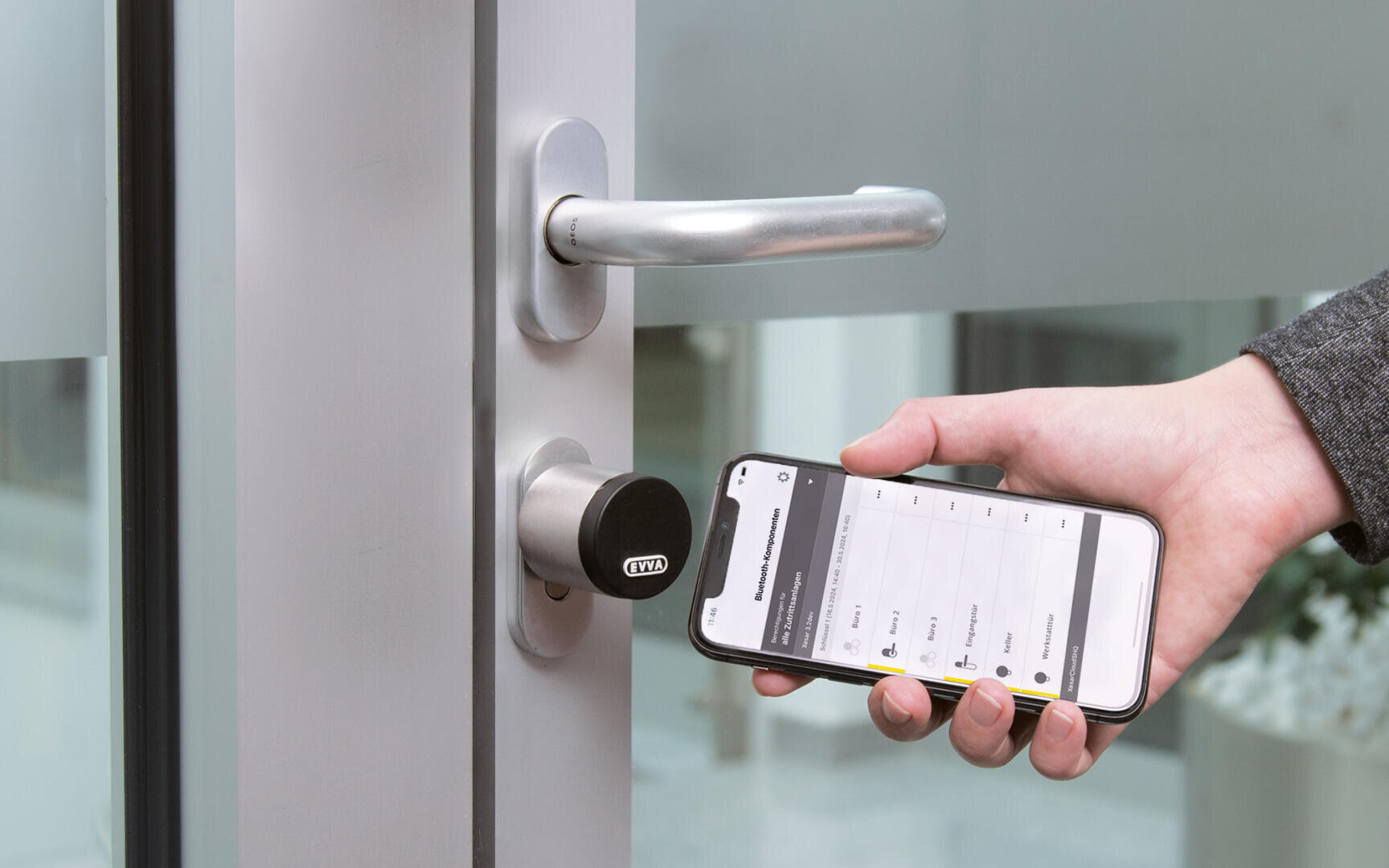 Eine Person hält ein Smartphone mit einer Smart-Lock-App offen und entriegelt damit eine moderne silberne Tür, die mit einem digitalen Schloss ausgestattet ist. Die Szene suggeriert den Einsatz mobiler Technologie für einen sicheren, schlüssellosen Zugang.