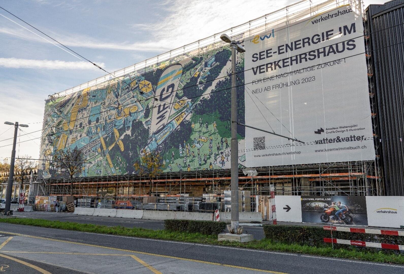 Ein großes, im Bau befindliches Gebäude ist mit Gerüsten und Schutznetzen bedeckt, auf denen farbenfrohe Wandmalereien und Banner für "SEE-ENERGIE IM VERKEHRSHAUS" und Informationen über bevorstehende Ausstellungen angebracht sind.