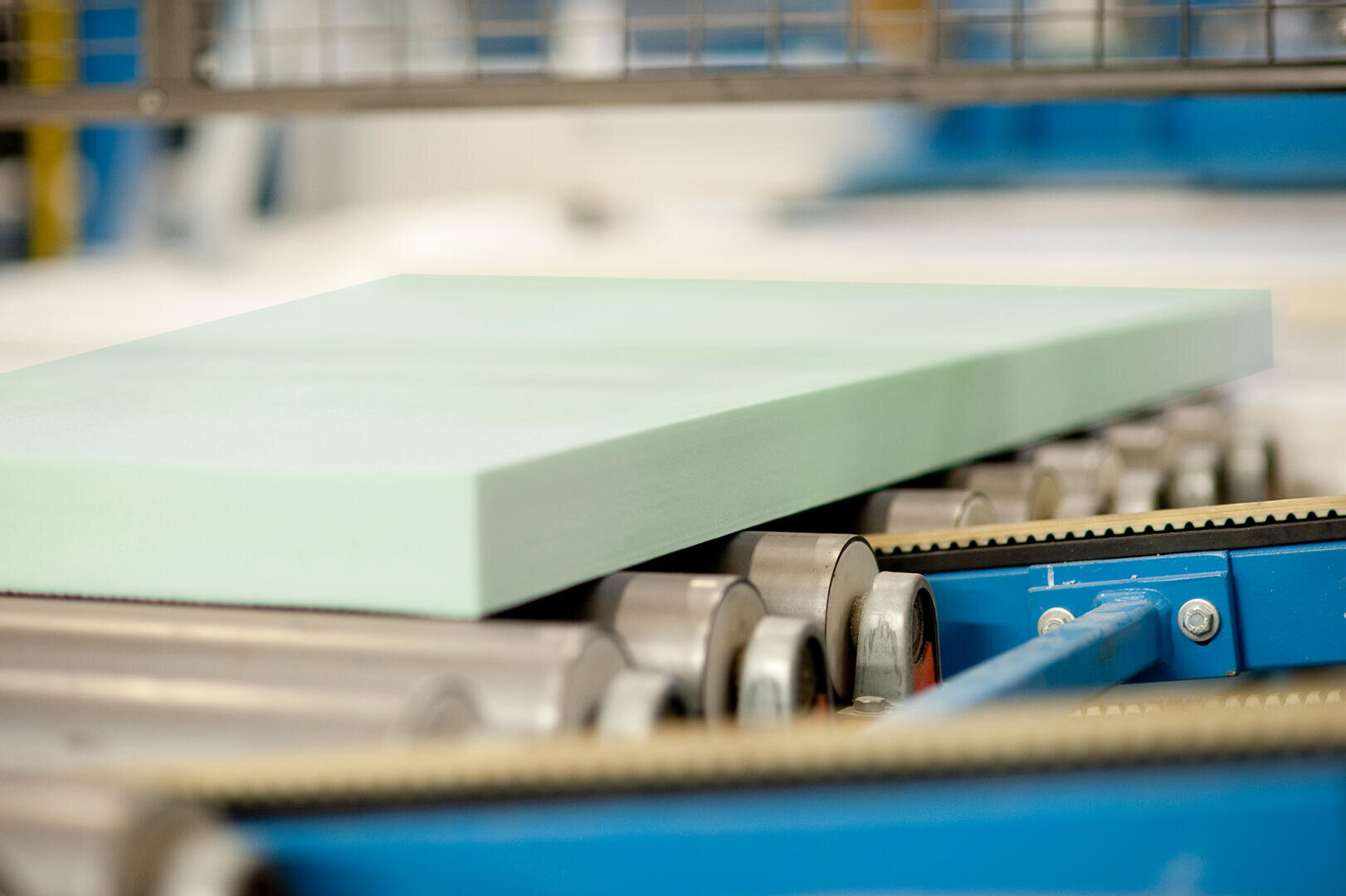 Eine hellgrüne Schaumstoffplatte bewegt sich auf einem Förderband in einer industriellen Umgebung, möglicherweise während einer Herstellungs- oder Verarbeitungsphase.