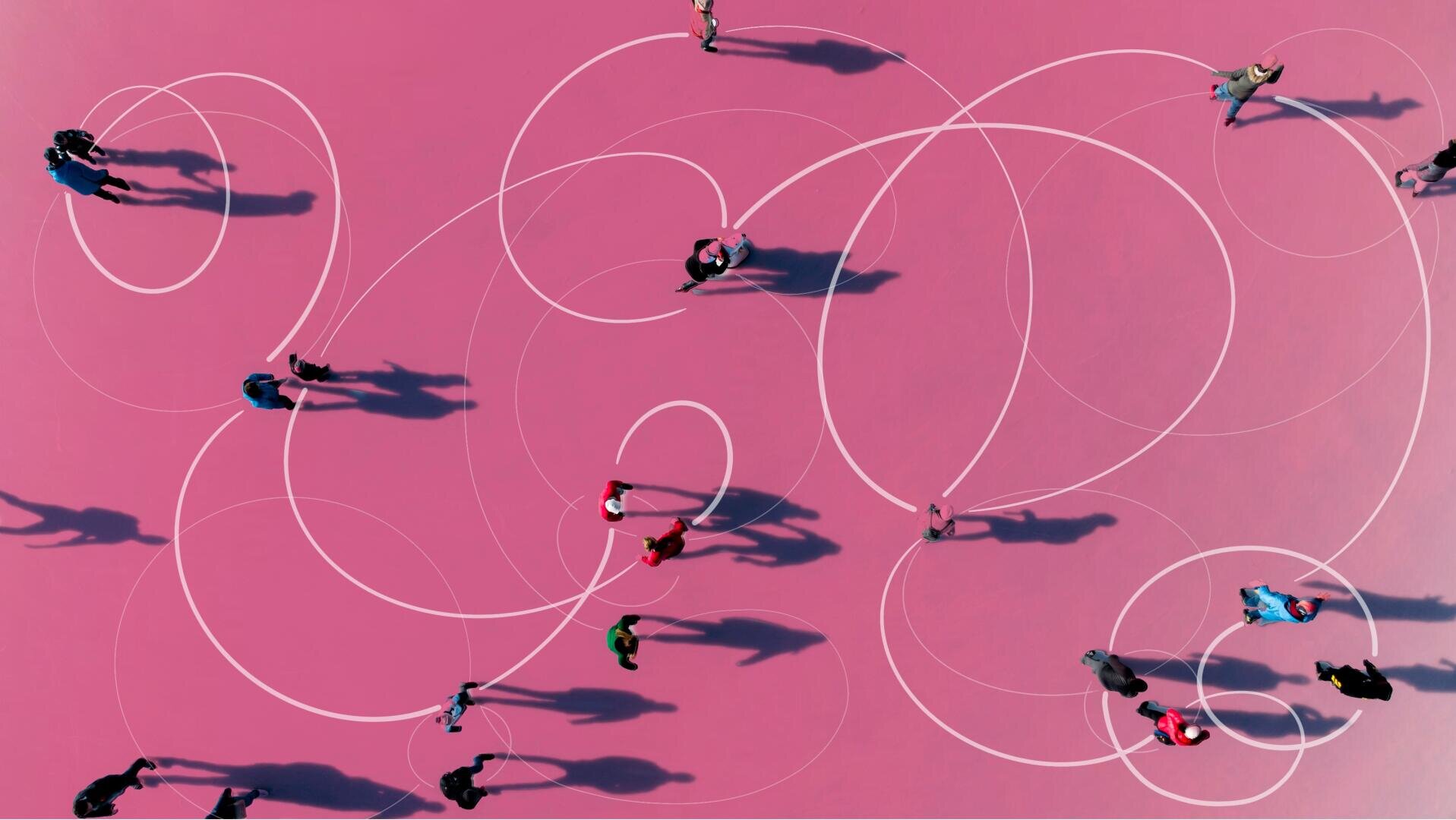 Luftaufnahme von Menschen, die auf einer rosafarbenen Fläche mit weißen, wirbelnden Linien gehen, die lange Schatten in verschiedene Richtungen werfen. Die Szene wirkt abstrakt und verspielt.
