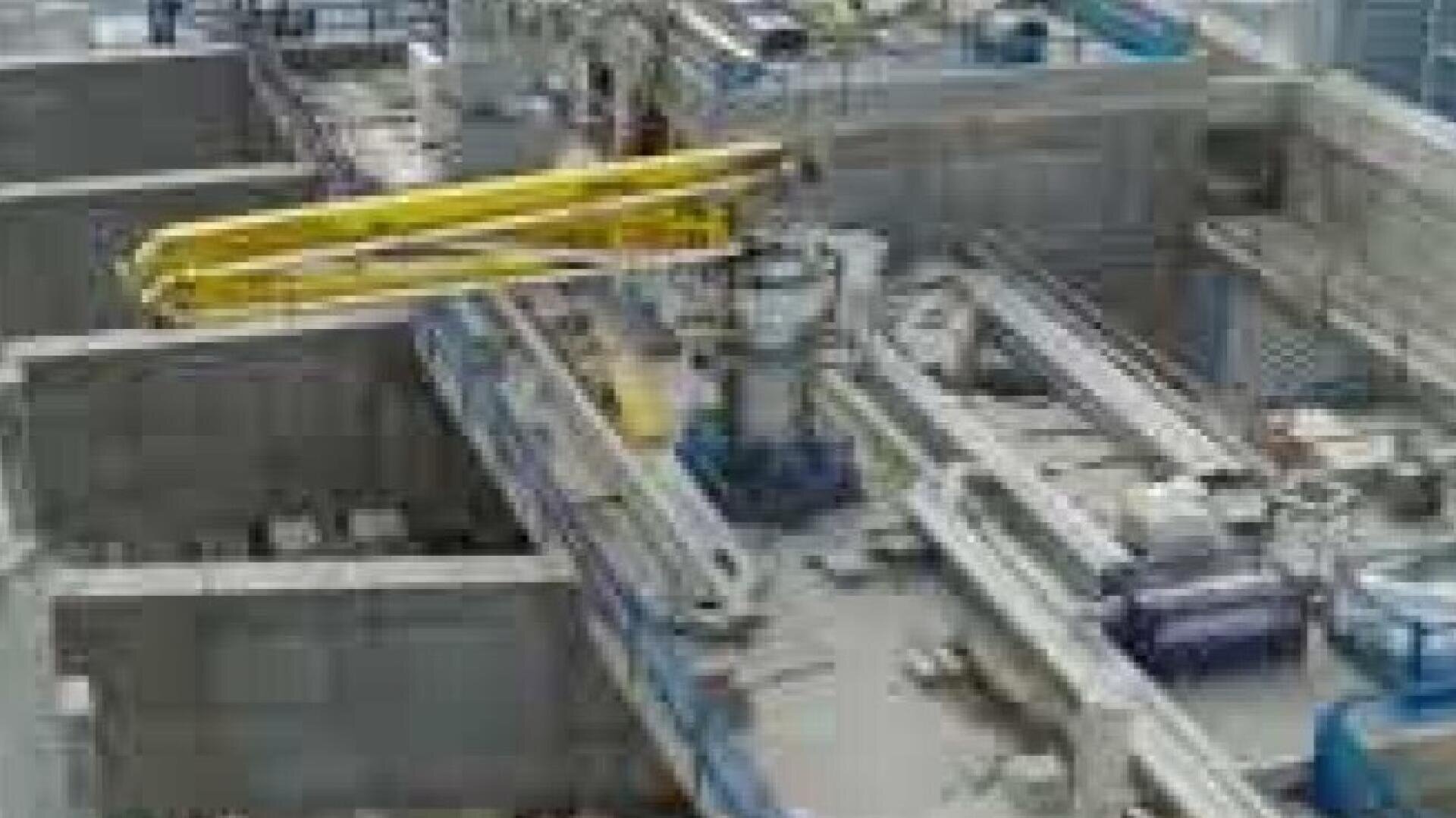 Eine große Industrieanlage mit Betontrennwänden, schweren Maschinen und gelben Brückenkränen, die wahrscheinlich für Fertigungs- oder Verarbeitungsprozesse genutzt wird.