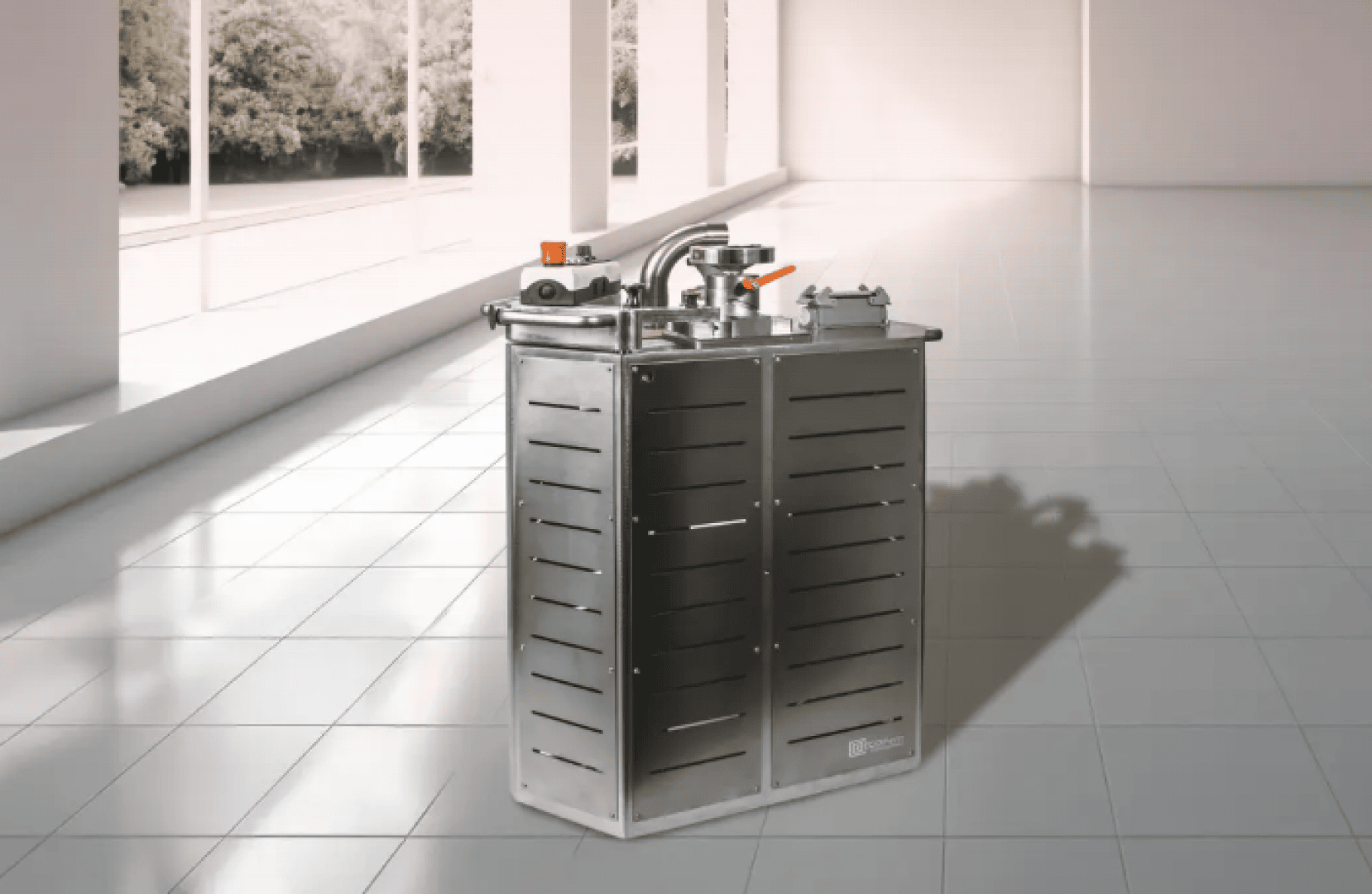 In einem hellen, modernen Raum mit großen Fenstern und Blick auf die Bäume im Freien steht eine Industriemaschine aus Edelstahl mit Lüftungsschlitzen und Bedienknöpfen auf einem glänzenden Fliesenboden.