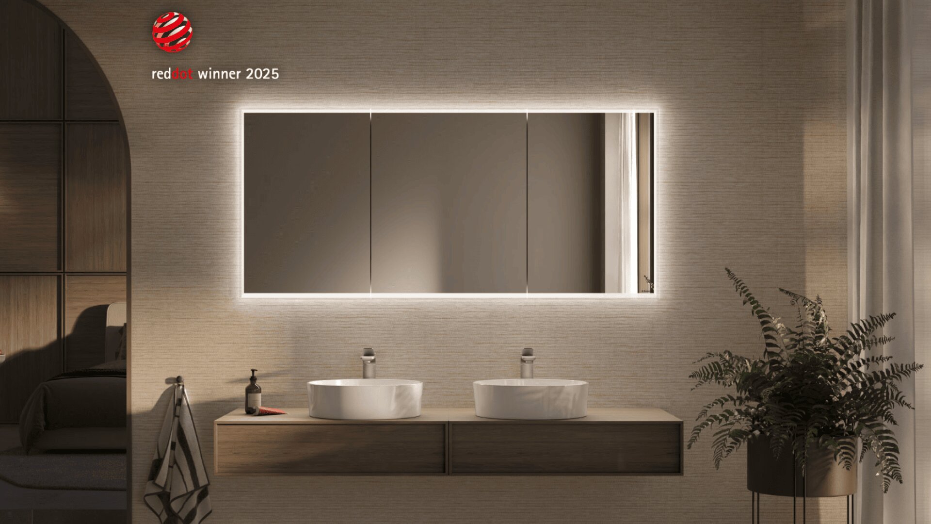 Modernes Badezimmer mit einem großen hinterleuchteten Spiegel über zwei runden Waschbecken auf einem hölzernen Waschtisch, einer Pflanze rechts, Seife und Handtuch links und einem Red Dot Award 2025-Logo an der oberen linken Wand.