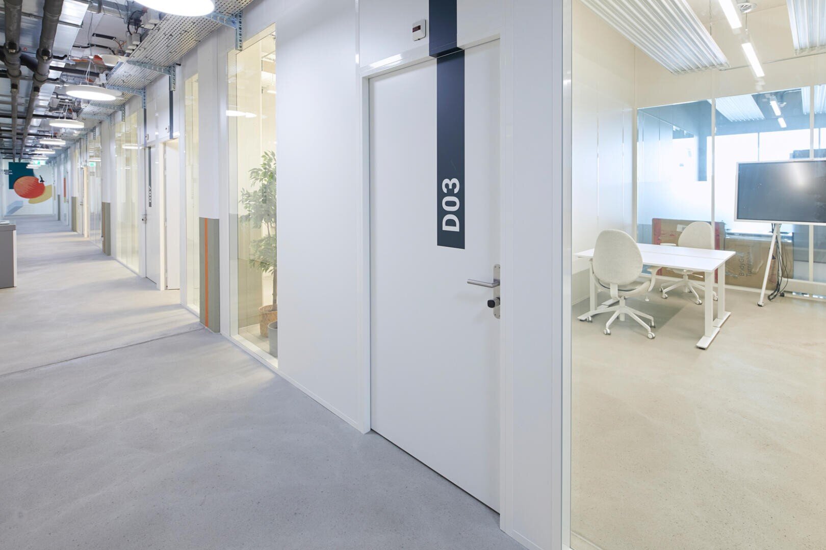 Couloir de bureau clair et moderne avec des salles de réunion vitrées, des portes blanches et un panneau D03 visible sur une porte ; des chaises et des tables vides sont visibles à travers les parois vitrées.