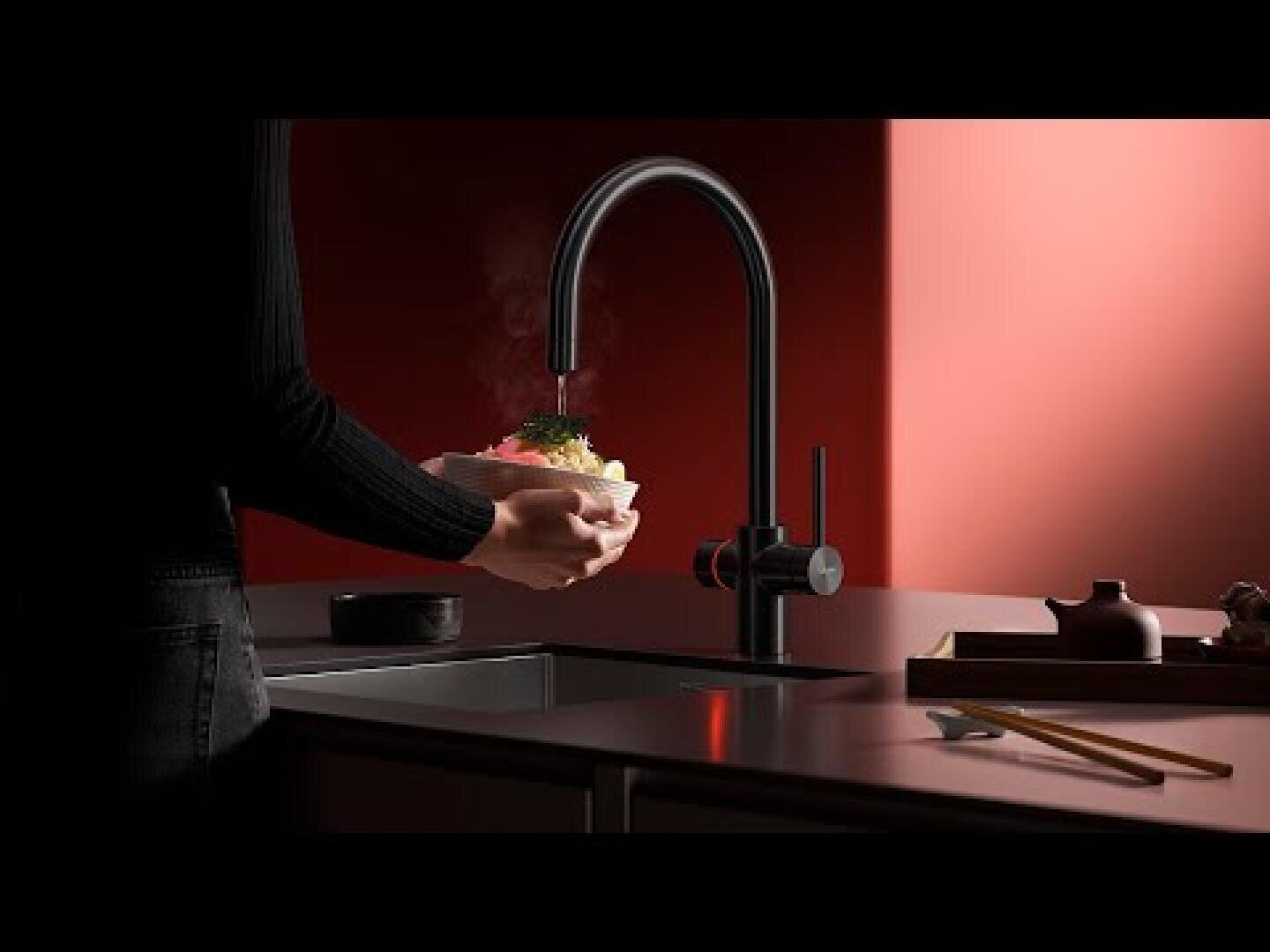 Eine Person hält eine dampfende Schüssel mit Essen unter einem modernen schwarzen Küchenwasserhahn, mit einem minimalistischen Waschbecken und einem roten Hintergrund, Stäbchen und Teekanne auf dem Tresen.