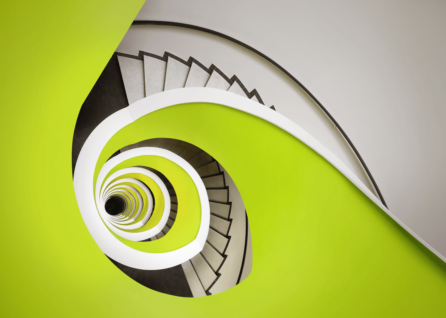 Spindeltreppe mit leuchtend grünen und weißen Akzenten, von oben fotografiert, wodurch ein visuell auffälliges, abstraktes Muster mit einem zentralen, runden Brennpunkt entsteht.