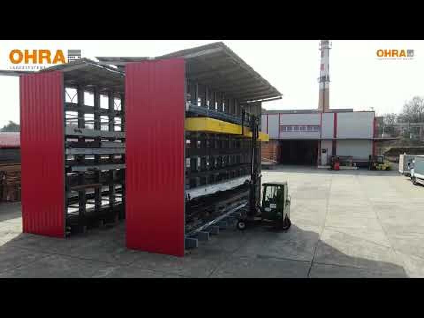 Un chariot élévateur roule à côté d'un grand rayonnage de stockage en plein air à plusieurs étages, en métal et aux parois latérales rouges, situé sur un site industriel. Le logo OHRA apparaît dans les coins de l'image.