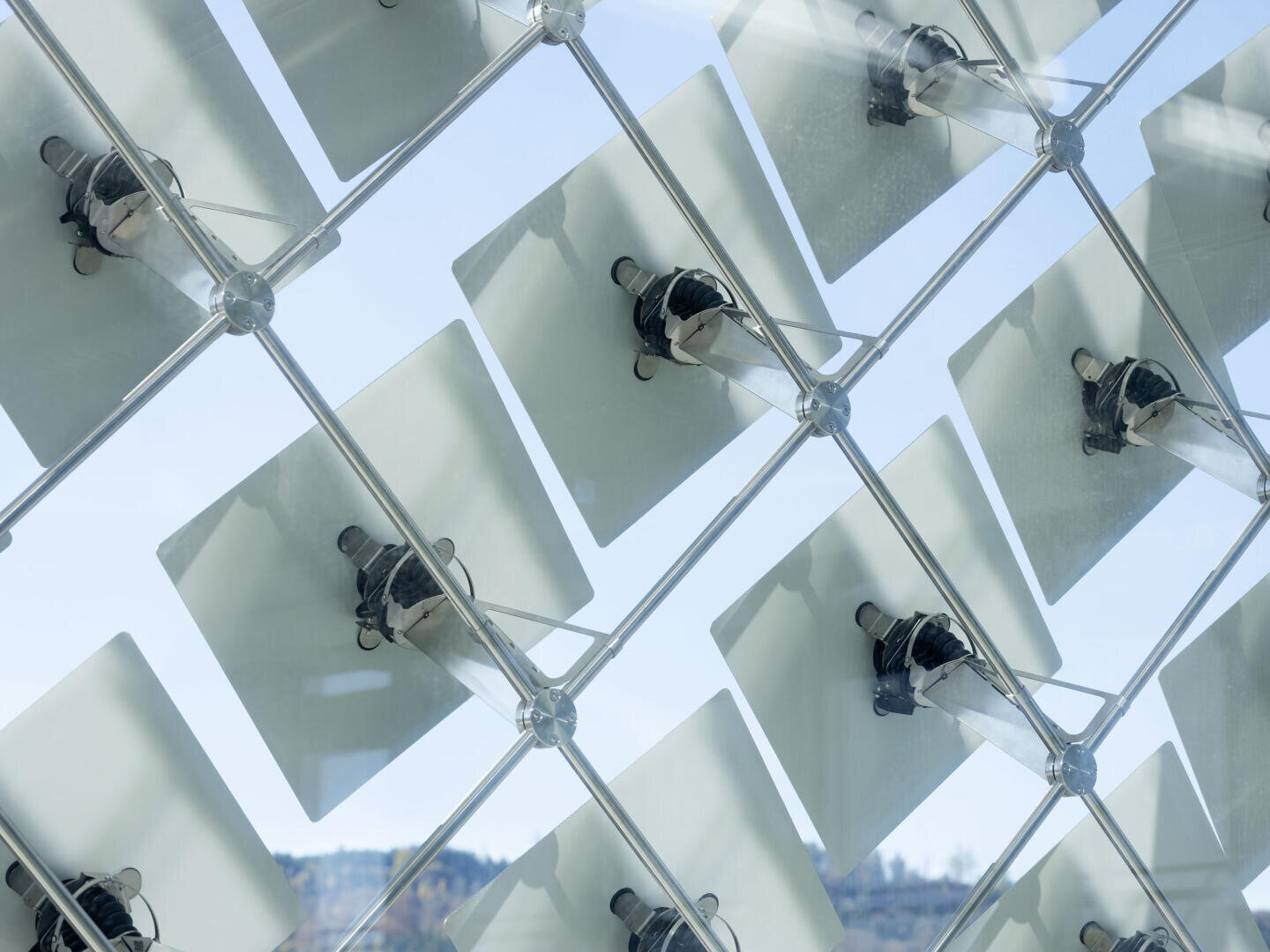 Un gros plan sur une grille géométrique de vitres carrées, chacune montée sur un cadre métallique, reflétant le ciel et le paysage à travers une structure architecturale moderne.