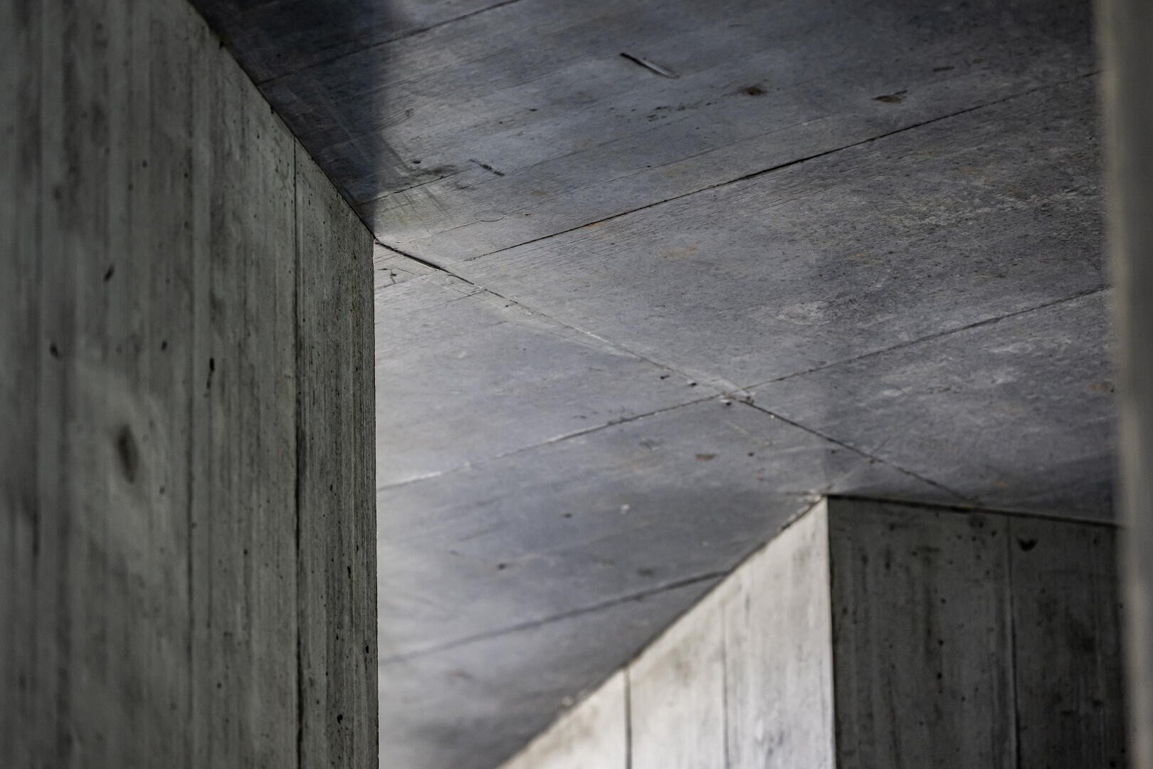 Nahaufnahme von sich kreuzenden Betonwänden und -decken, die scharfe Winkel und strukturierte Oberflächen in einer modernen architektonischen Struktur zeigen.