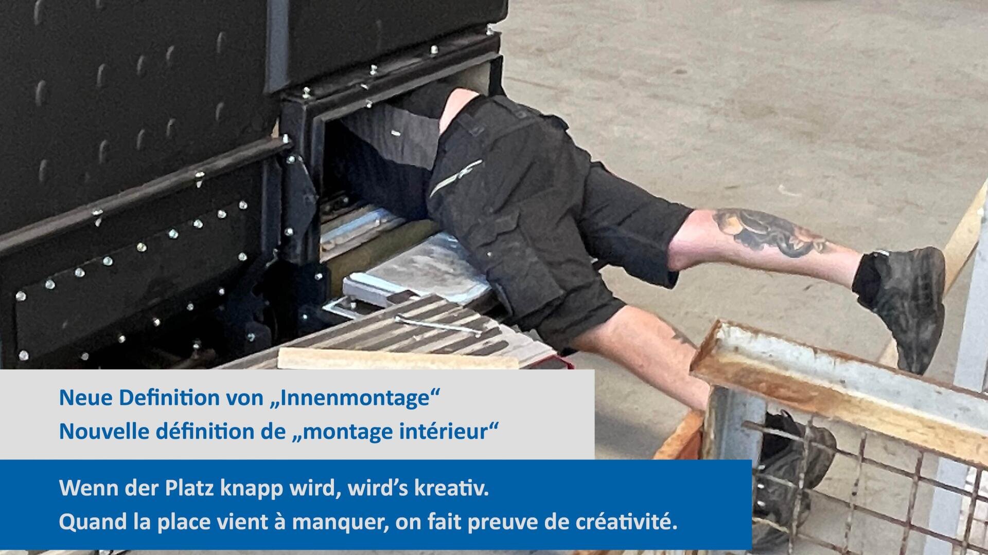 Eine Person mit tätowierten Beinen krabbelt kopfüber in eine kleine, dunkle industrielle Maschinenöffnung und arbeitet auf engem Raum. Der Text auf Deutsch und Französisch erklärt die Kreativität bei begrenztem Platz.
