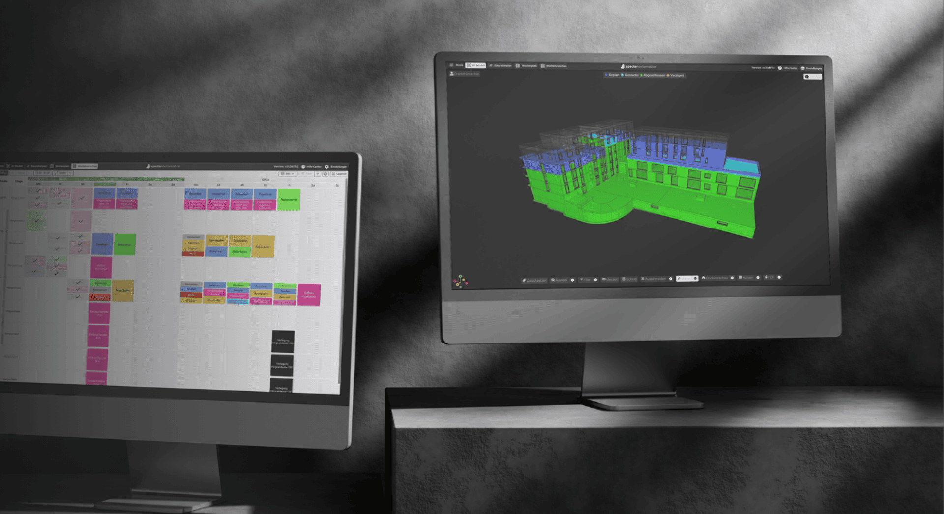 Zwei Computermonitore auf einem Schreibtisch; der linke Bildschirm zeigt einen bunten Kalender oder Zeitplan, während der rechte Bildschirm ein 3D-Gebäudemodell in Grün und Blau auf dunklem Hintergrund zeigt.