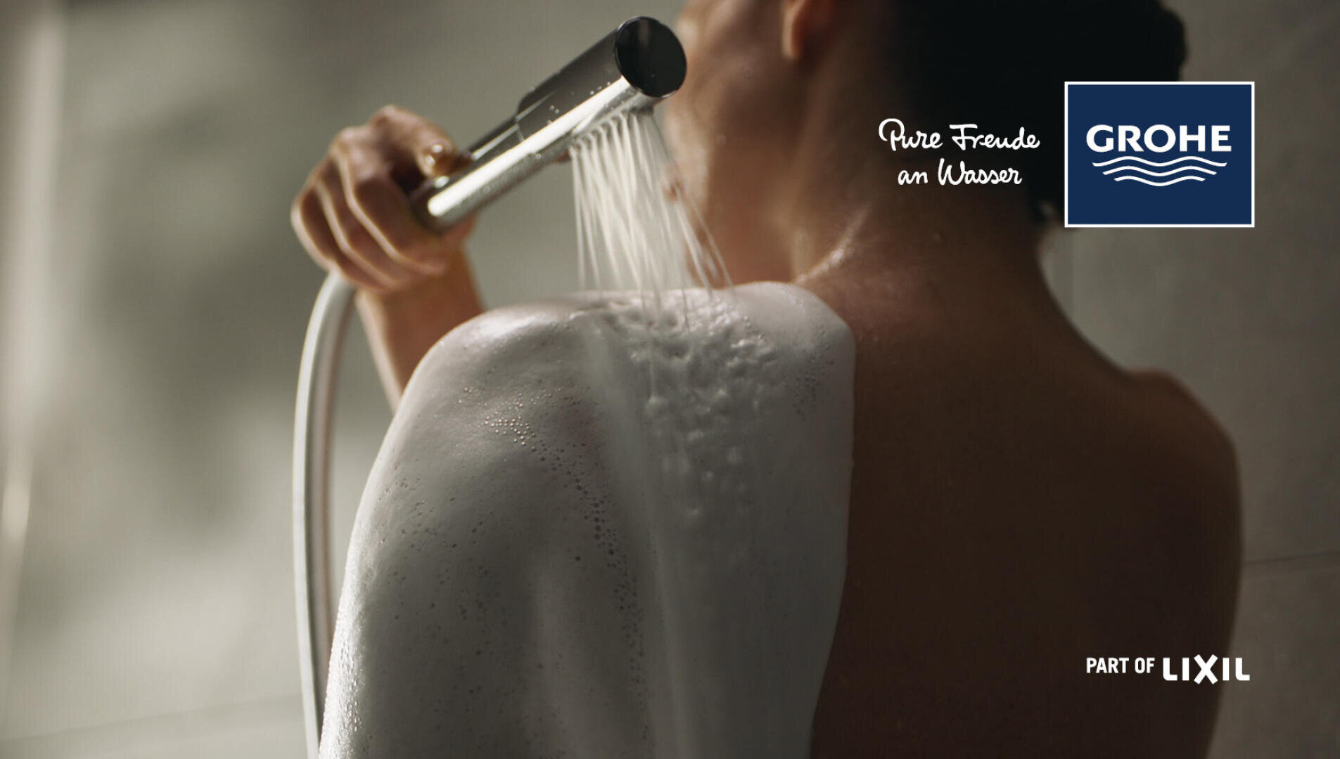 Eine Person duscht und spült sich mit einer Handbrause den Seifenschaum von den Schultern. Das GROHE Logo und der Text Pure Freude an Wasser erscheinen in der oberen rechten Ecke, zusammen mit Part of LIXIL am unteren Rand.