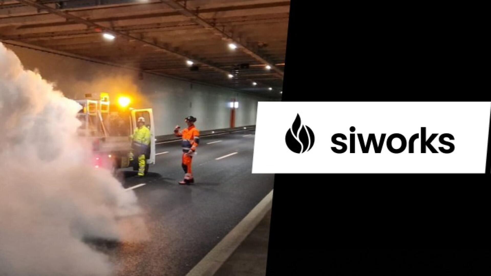 Zwei Arbeiter in Schutzkleidung stehen auf einer Straße in einem mit dichtem Rauch gefüllten Tunnel, neben einem Fahrzeug mit Blinklichtern. Auf der rechten Seite des Bildes ist das siworks-Logo mit einem Flammensymbol zu sehen.