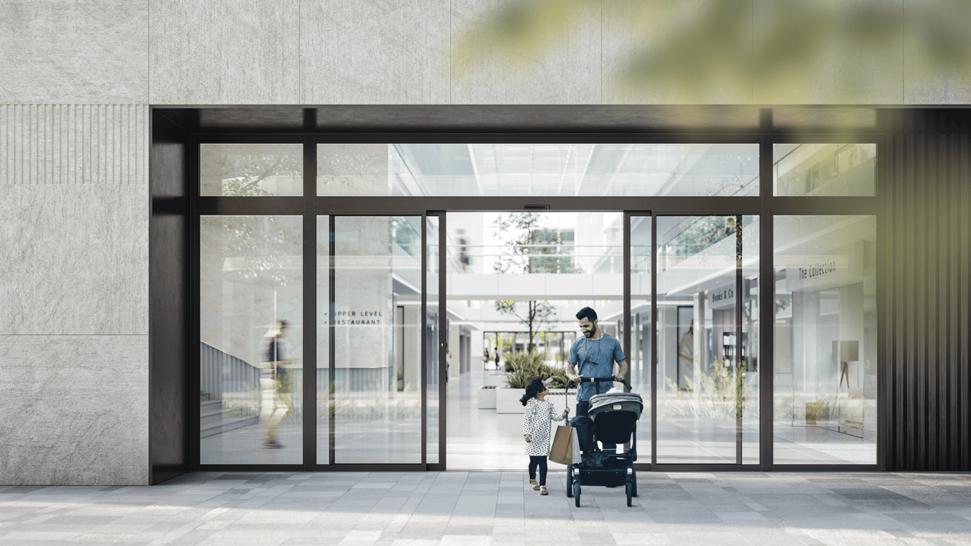 Ein Mann mit einem Kinderwagen und ein junges Mädchen mit einer Einkaufstasche stehen vor den Glastüren eines modernen Einkaufszentrums, in dem unscharfe Menschen und Grünflächen zu sehen sind.