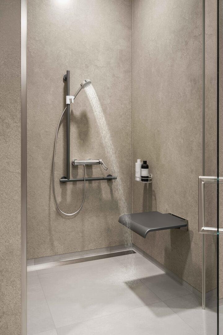 Barrierefreie Dusche mit einem an der Wand befestigten Sitz, einer Handbrause, Haltegriffen und eingebauten Regalen für Toilettenartikel; minimalistisches Design mit grauen Fliesen und einem offenen, begehbaren Eingang.