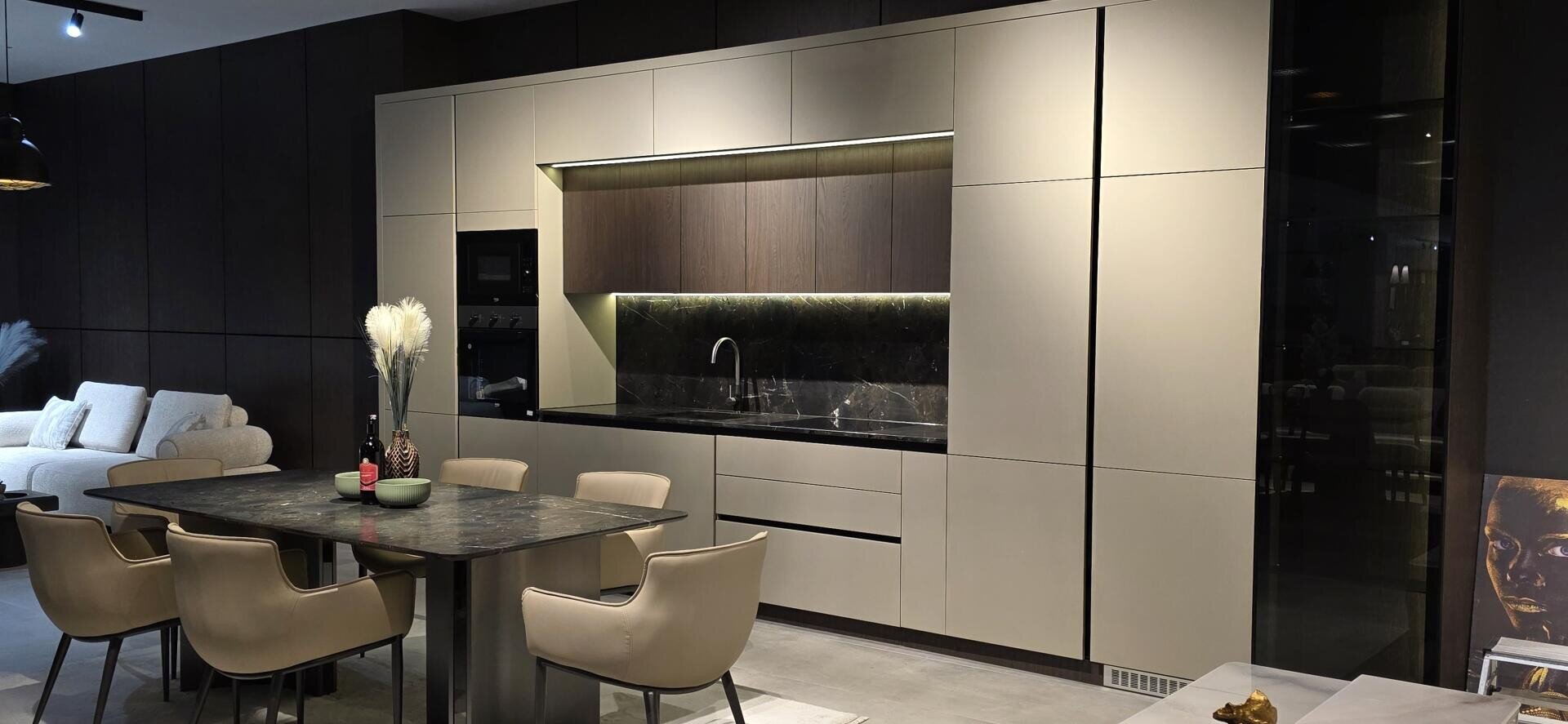 Cuisine moderne avec armoires beiges, appareils encastrés, dosseret en marbre noir et coin repas avec table en marbre et chaises crème. Des vases décoratifs et des œuvres d'art ajoutent une touche de style à cet espace épuré.