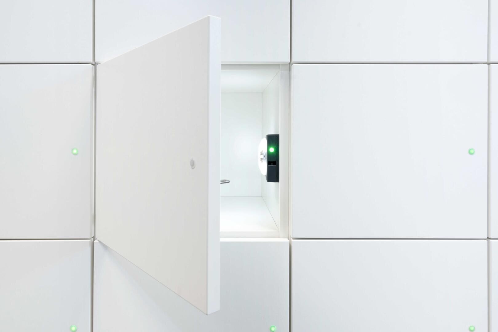 Une armoire blanche avec une porte ouverte qui laisse apparaître un compartiment clair et vide à l'intérieur. L'armoire a un design épuré et minimaliste avec de petits témoins lumineux verts sur les portes fermées.