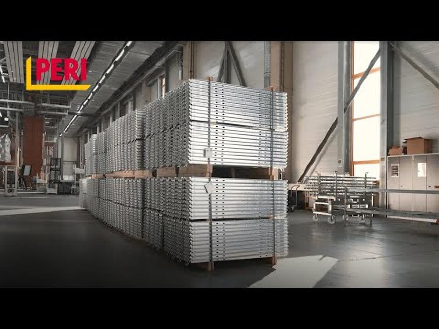 Dans un entrepôt industriel spacieux et bien éclairé, les panneaux métalliques sont empilés de manière ordonnée sur des palettes en bois. Dans le coin supérieur gauche, on peut voir le logo rouge et jaune de PERI.