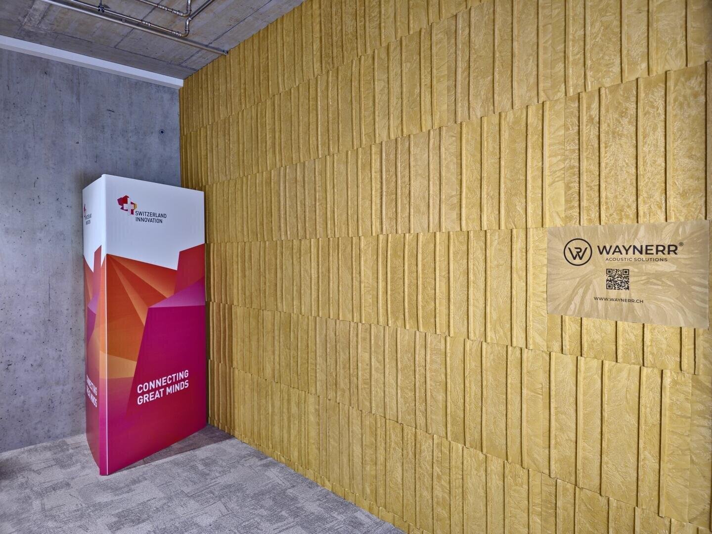 Une pièce moderne avec un mur jaune texturé, un code QR et le logo "WAYNERR", et un présentoir rectangulaire coloré avec des motifs géométriques et le texte "CONNECTIONS CREATE GREAT MINDS".