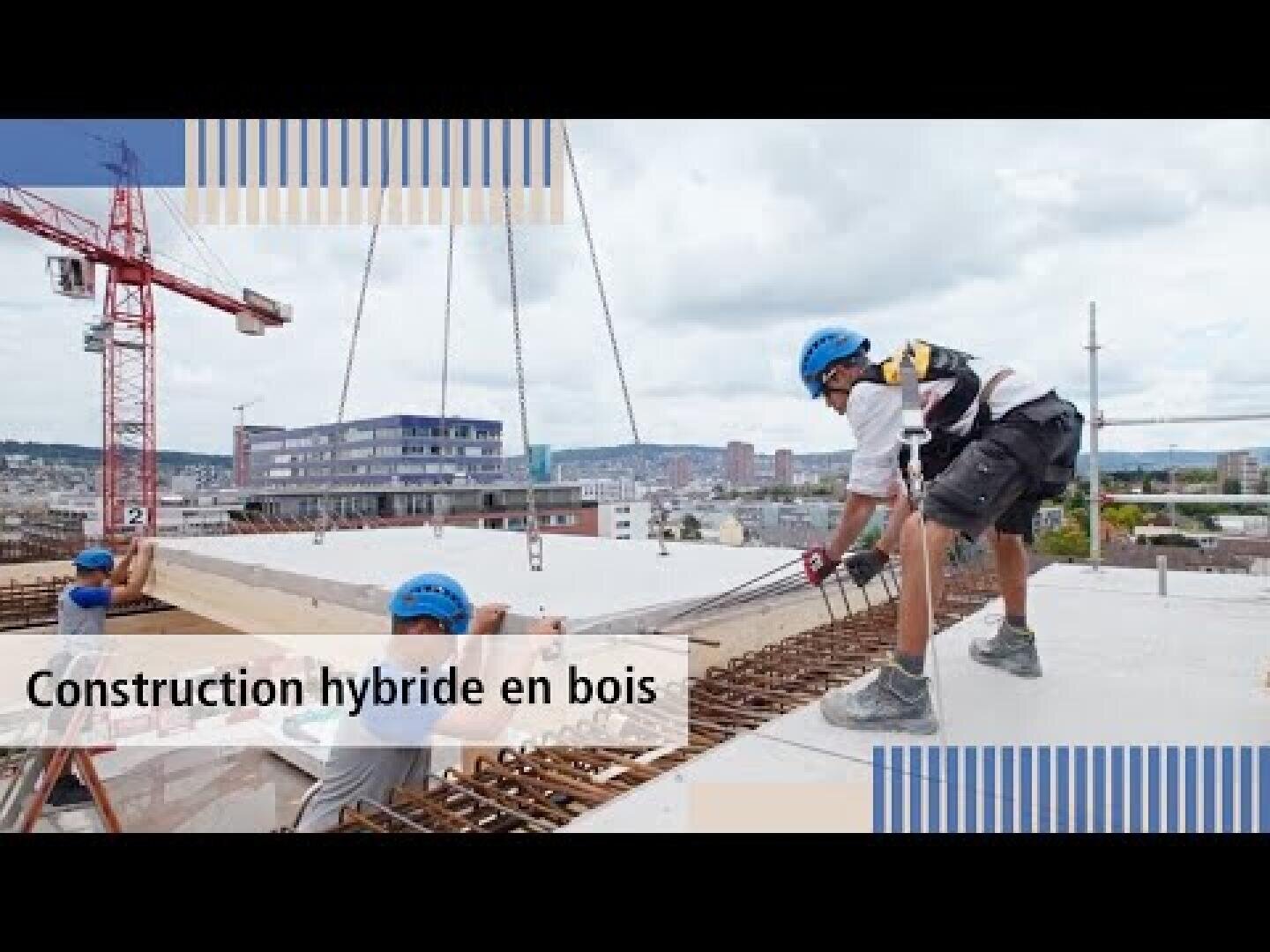 Des ouvriers portant des casques installent un grand panneau de bois sur un chantier de construction avec des grues et des bâtiments urbains en arrière-plan. Le texte se lit comme suit : Construction hybride en bois.