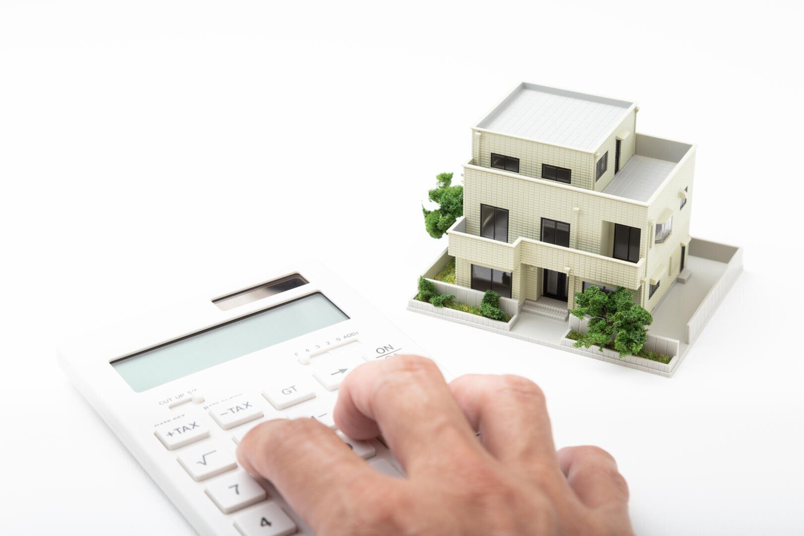 Eine Hand drückt Knöpfe auf einem Taschenrechner neben einem kleinen Modell eines modernen Hauses, was Immobilienberechnungen oder die Planung des Haushaltsbudgets symbolisiert.