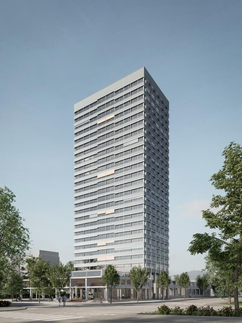 Ein hohes, modernes Hochhaus mit vielen Fenstern steht vor einem klaren blauen Himmel, umgeben von Bäumen und kleineren Gebäuden auf Straßenniveau.