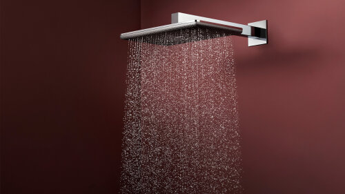 Ein moderner, quadratischer, verchromter Duschkopf, der an einer kastanienbraunen Wand montiert ist und einen stetigen Strahl von Wassertropfen in einem Regenmuster abgibt.