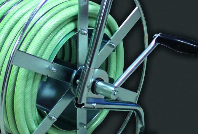 Nahaufnahme einer Schlauchtrommel aus Metall, um die ein grüner Schlauch gewickelt ist, mit einem schwarzen Griff zum Aufwickeln, vor einem dunklen Hintergrund.