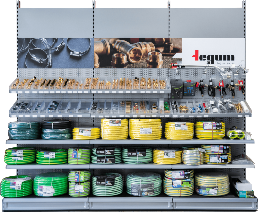 Ein Ladenregal mit grünen und gelben Gartenschläuchen, Schlauchanschlüssen, Metallschellen, Düsen und Armaturen. Auf der oberen Platte sind Abbildungen von Sanitärteilen und das Logo der Marke Tegum zu sehen.