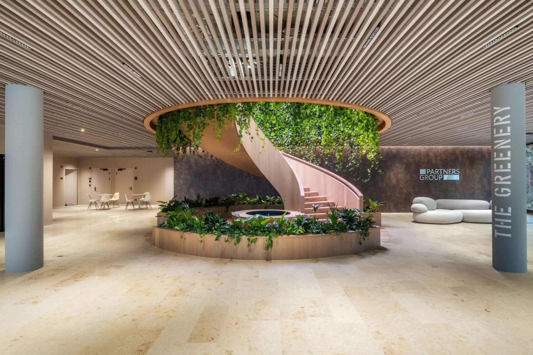 Un hall de bureau moderne avec un escalier en colimaçon orné de plantes vertes suspendues, une jardinière ronde remplie de plantes, des meubles minimalistes et un panneau indiquant "Partners Group" et "The Greenery" sur le mur.